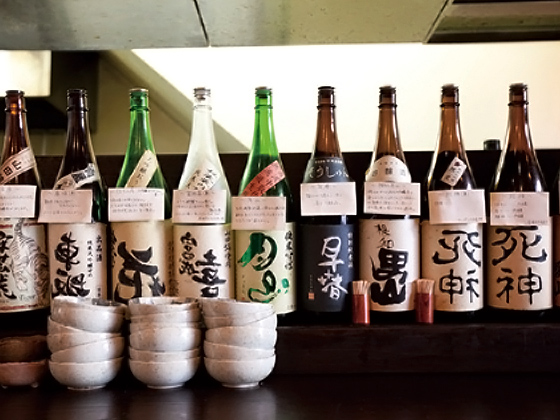 「日本酒って一番完成された酒だと思うんだよね。だからそのおいしさをもっと広めたい」。店内にはざっと320本の一升瓶が飾られ、その一つひとつに特徴や呑み方が書かれた田中さんのコメントがついている。壮観！